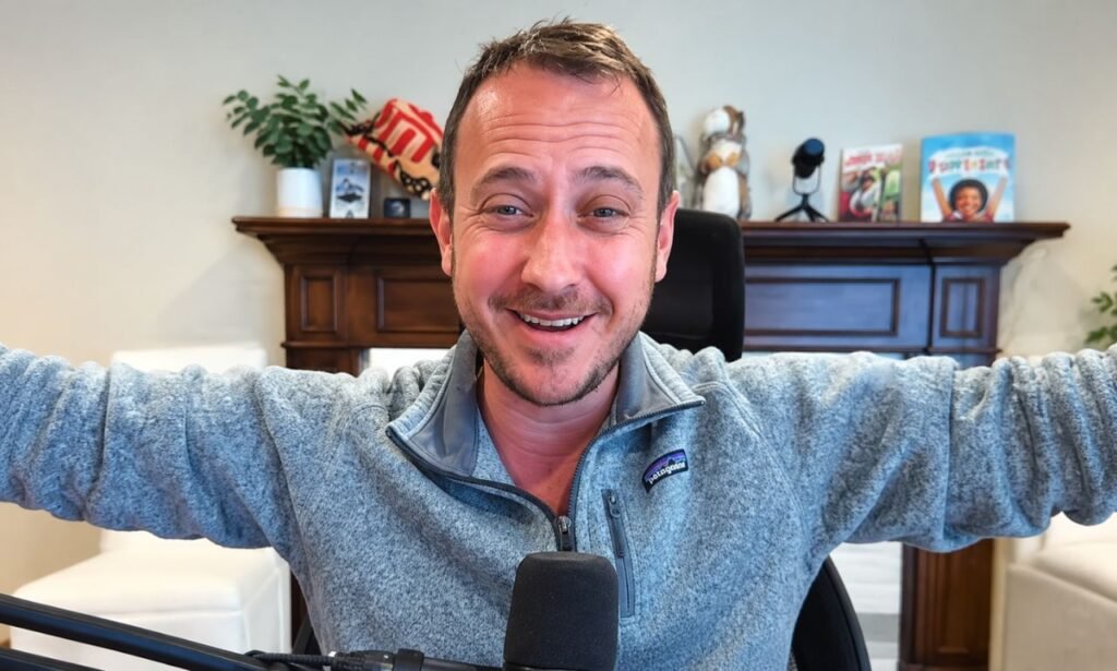 Ben Meiselas smiling during a video recording in his home office, wearing a gray quarter-zip fleece with a microphone in front of him.
