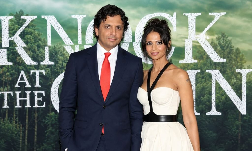 Bhavna Vaswani and M. Night Shyamalan posing together at a red-carpet premiere in formal attire.