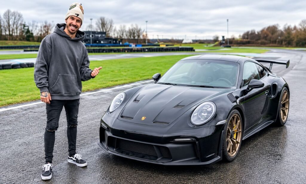 Mat Armstrong standing beside a black Porsche sports car on a wet racetrack.