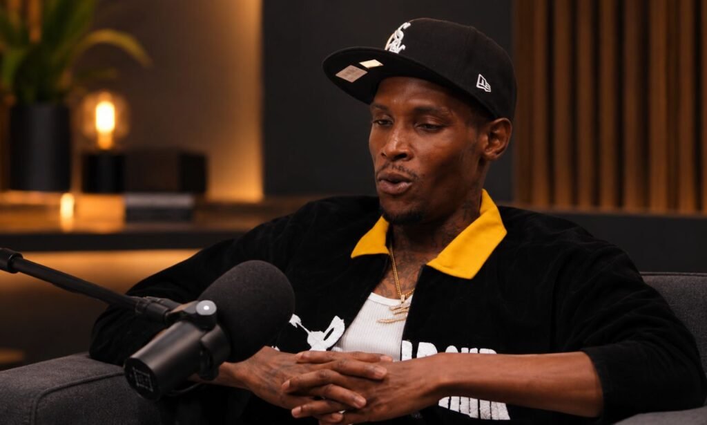 Jadarius Jenkins wearing a black cap and black jacket with a yellow collar during a podcast interview.