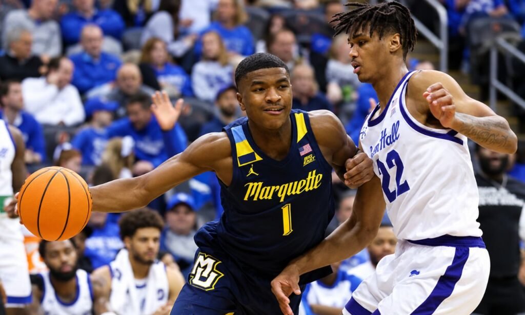 Marquette basketball player Davon dribbling the ball past a Seton Hall defender during an intense college basketball game in a packed indoor arena.