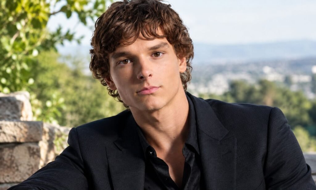 Mason Thames in a black suit posing outdoors with a blurred city and greenery in the background.