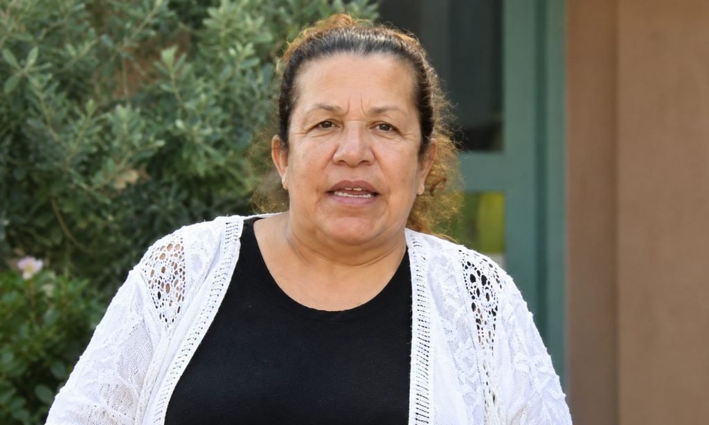 Mildred Patricia Baena wearing a white embroidered cardigan over a black top in an outdoor setting with greenery in the background.