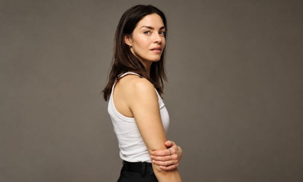 Natalie Madueño in a white sleeveless top posing for a professional studio portrait against a neutral gray background.