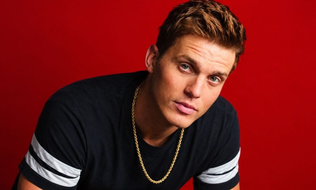 Parker McCollum posing in a black shirt and gold chain against a red studio background.