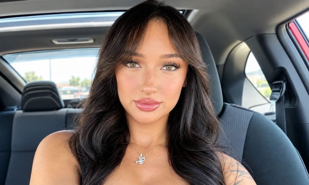 Rhegan Coursey smiling for a selfie inside a car, wearing a necklace and showing her long dark wavy hair.