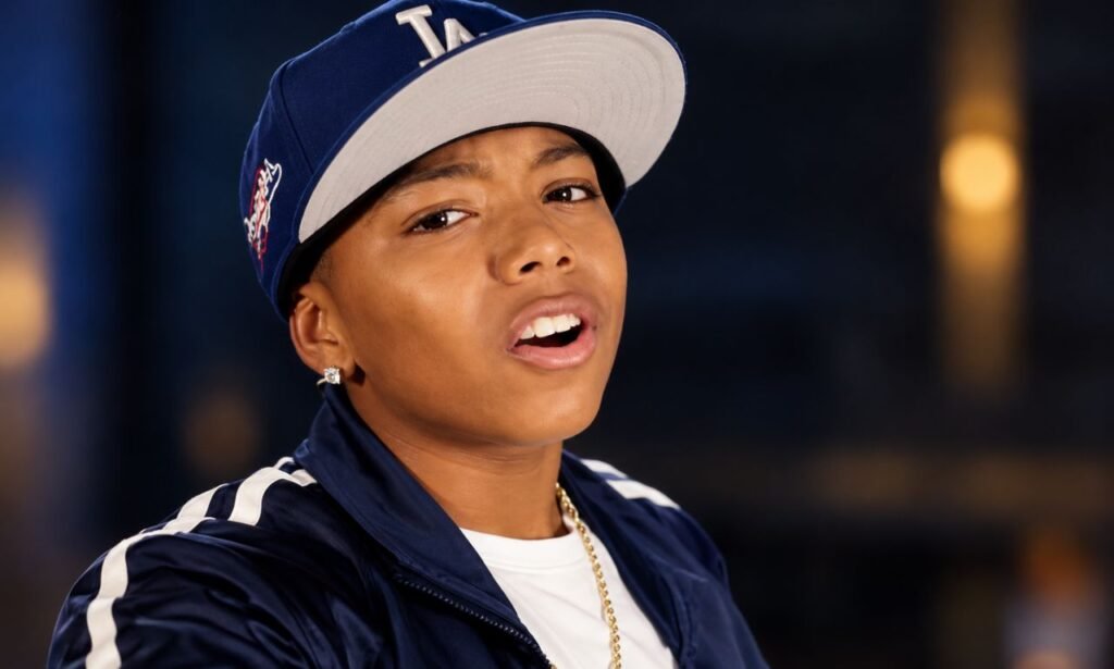 Thaddeus J. Mixson posing in a navy baseball cap and jacket with a gold chain in a cinematic close-up portrait.